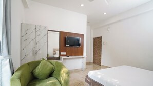 A modern hotel room with a green sofa, a bed, a flat-screen TV mounted on a wooden panel, and a marble floor. - Hotel Royal Beach Exotica (Kanthi)