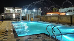 A swimming pool with water jets, a tiled deck, and buildings in the background. - Hotel Royal Beach Exotica (Kanthi)