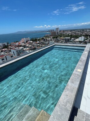 A clear blue swimming pool with a view of a coastal cityscape and mountains in the distance. - Casa ROMÁNtica: NEW modern 1-bedroom with ocean views (Puerto Vallarta)