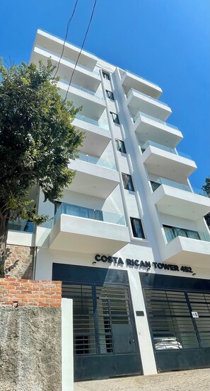 A modern building with multiple balconies, a sign reading 'Costa Rican Tower 452,' and a brick wall at the base. - Casa ROMÁNtica: NEW modern 1-bedroom with ocean views (Puerto Vallarta)