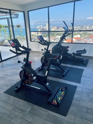 Una palestra con due cyclette, un vogatore e un tappetino per yoga.