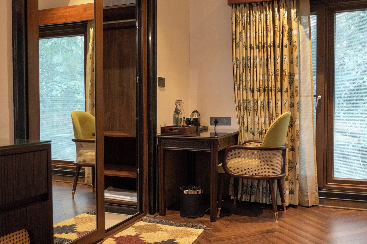 A room with a wooden desk, two chairs, a trash bin, and a window with curtains.