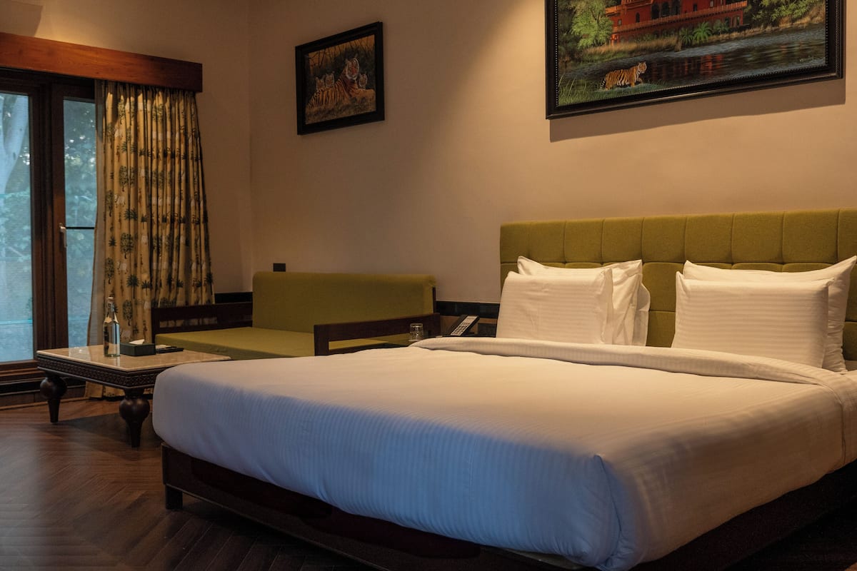 Une chambre d’hôtel avec un grand lit, un canapé vert, une petite table avec une bouteille et deux tableaux accrochés au mur.