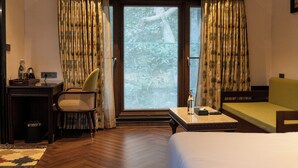 A hotel room with a bed, a desk, a chair, a sofa, and a window with curtains. - The Farm Stay by Aamaghati (Sawai Madhopur)