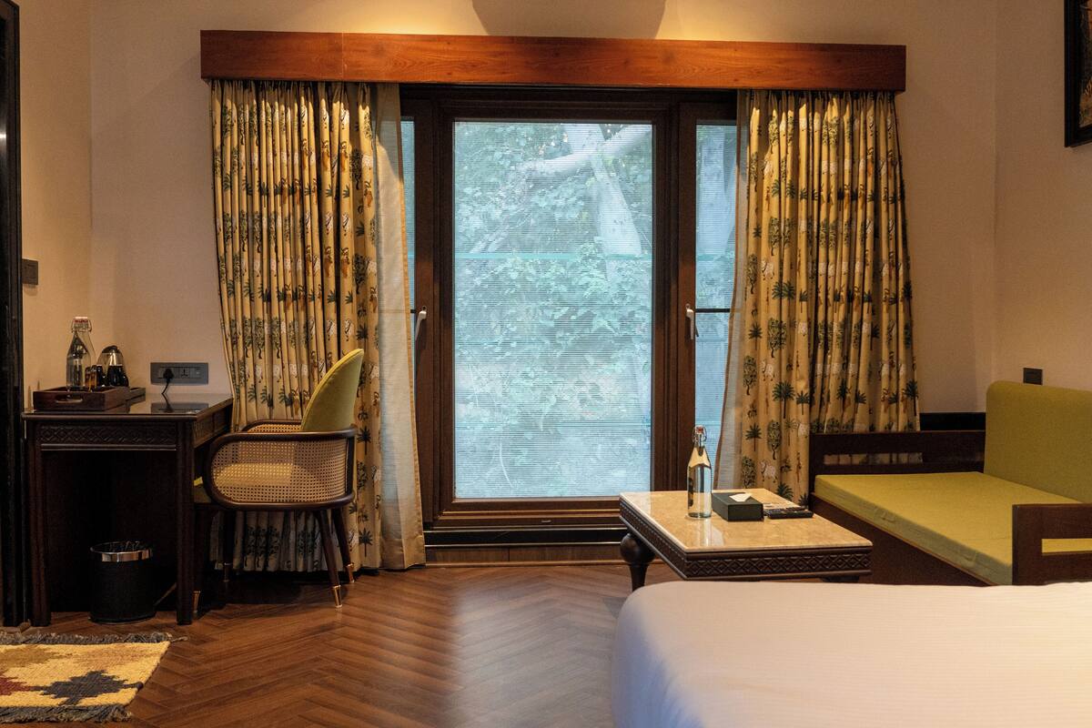 Une chambre d’hôtel avec un lit, un bureau, une chaise, un canapé et une fenêtre avec des rideaux.