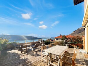 A wooden deck with outdoor furniture, a table, and chairs, overlooking a body of water and a mountainous landscape. - A gem nestled between the lake and the mountains (Veyrier-du-Lac)