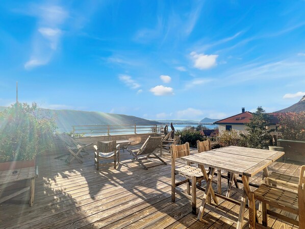 A wooden deck with a table and chairs, overlooking a body of water and hills. - A gem nestled between the lake and the mountains (Veyrier-du-Lac)