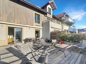 A wooden deck with outdoor furniture, a sliding glass door entrance, and a view of a residential building with a balcony. - A gem nestled between the lake and the mountains (Veyrier-du-Lac)
