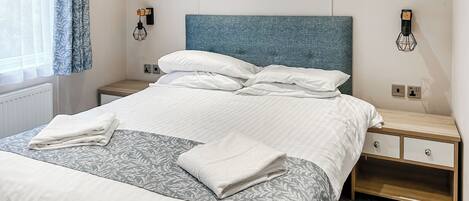 A neatly made bed with white linens, a blue headboard, and a bedside table with a lamp.