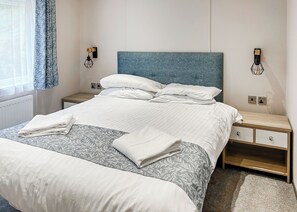 A neatly made bed with white linens, a blue headboard, and a bedside table with a lamp.