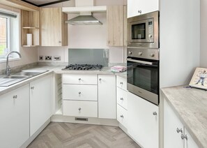 A modern kitchen with white cabinets, stainless steel appliances, and a herringbone-patterned floor.