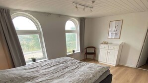 A bedroom with a bed, two windows, a chair, a cabinet, and a wall with a framed picture. - Spacious country home near forest and border (Padborg)