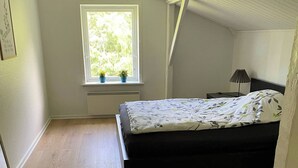 A bedroom with a bed, a window with plants, a nightstand, and a lamp. - Spacious country home near forest and border (Padborg)