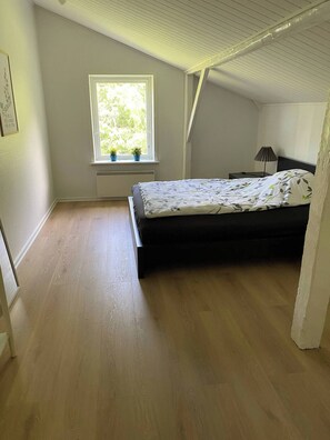 A bedroom with a bed, a window with plants, a nightstand, and a lamp. - Spacious country home near forest and border (Padborg)