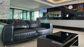 Een moderne lobby met een zwarte leren bank, een glazen salontafel en een receptiebalie met een klok en kleurrijke kunstwerken.