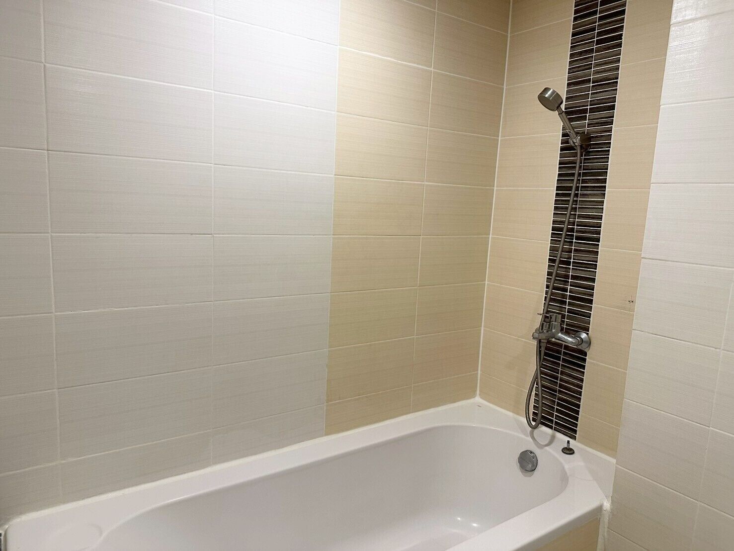 A standard bathtub with a showerhead and a control panel, surrounded by beige tiles.