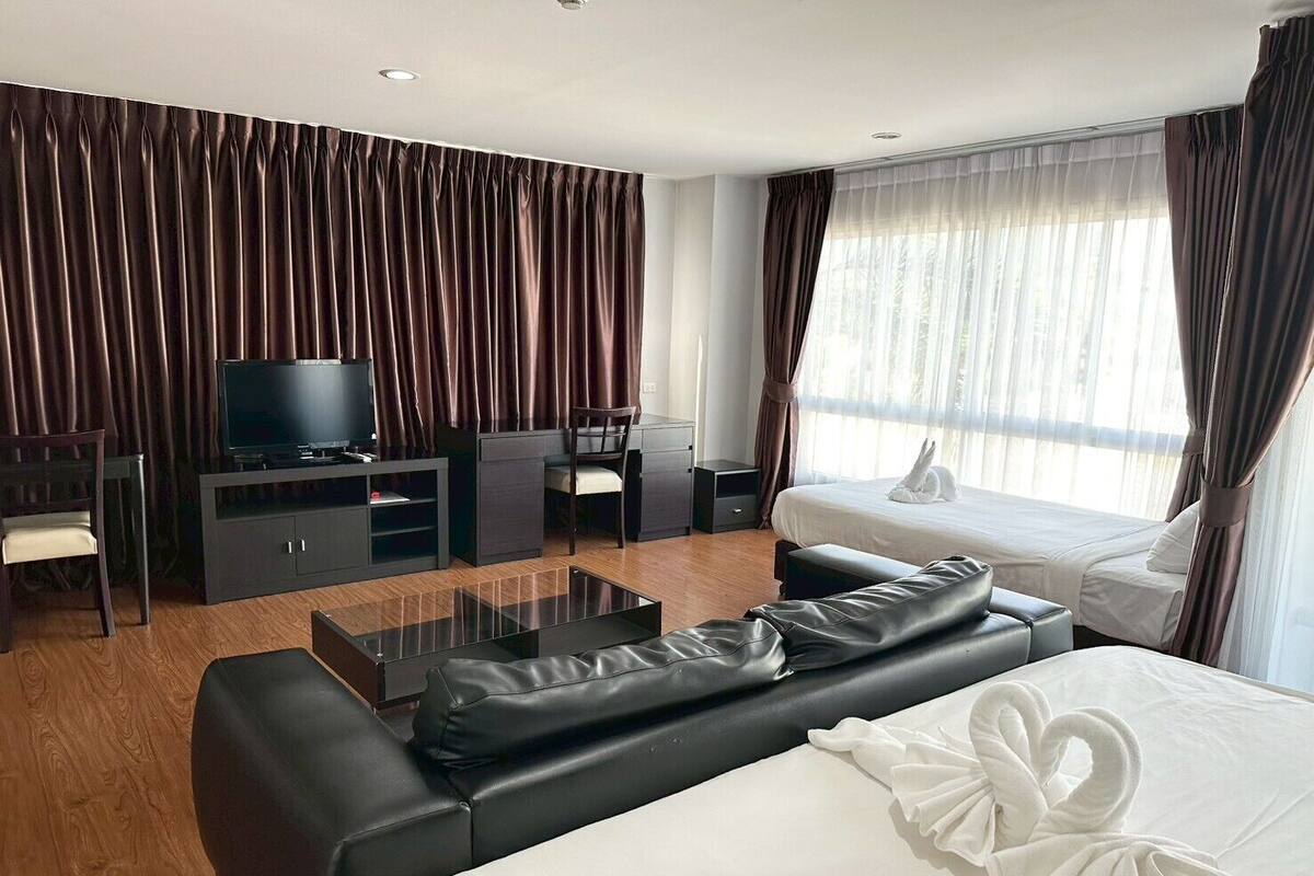 Een hotelkamer met een groot bed, een televisie op een standaard, een bureau met stoel, en een raam met gordijnen.