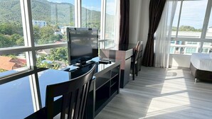 Een moderne hotelkamer met een groot raam, een bureau met een computer, een stoel en een bed.