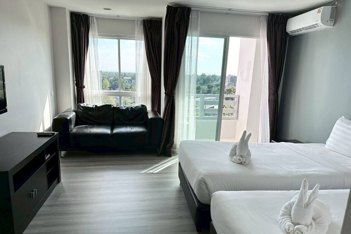 Een hotelkamer met een bed, een bank, een televisie en uitzicht over de stad.