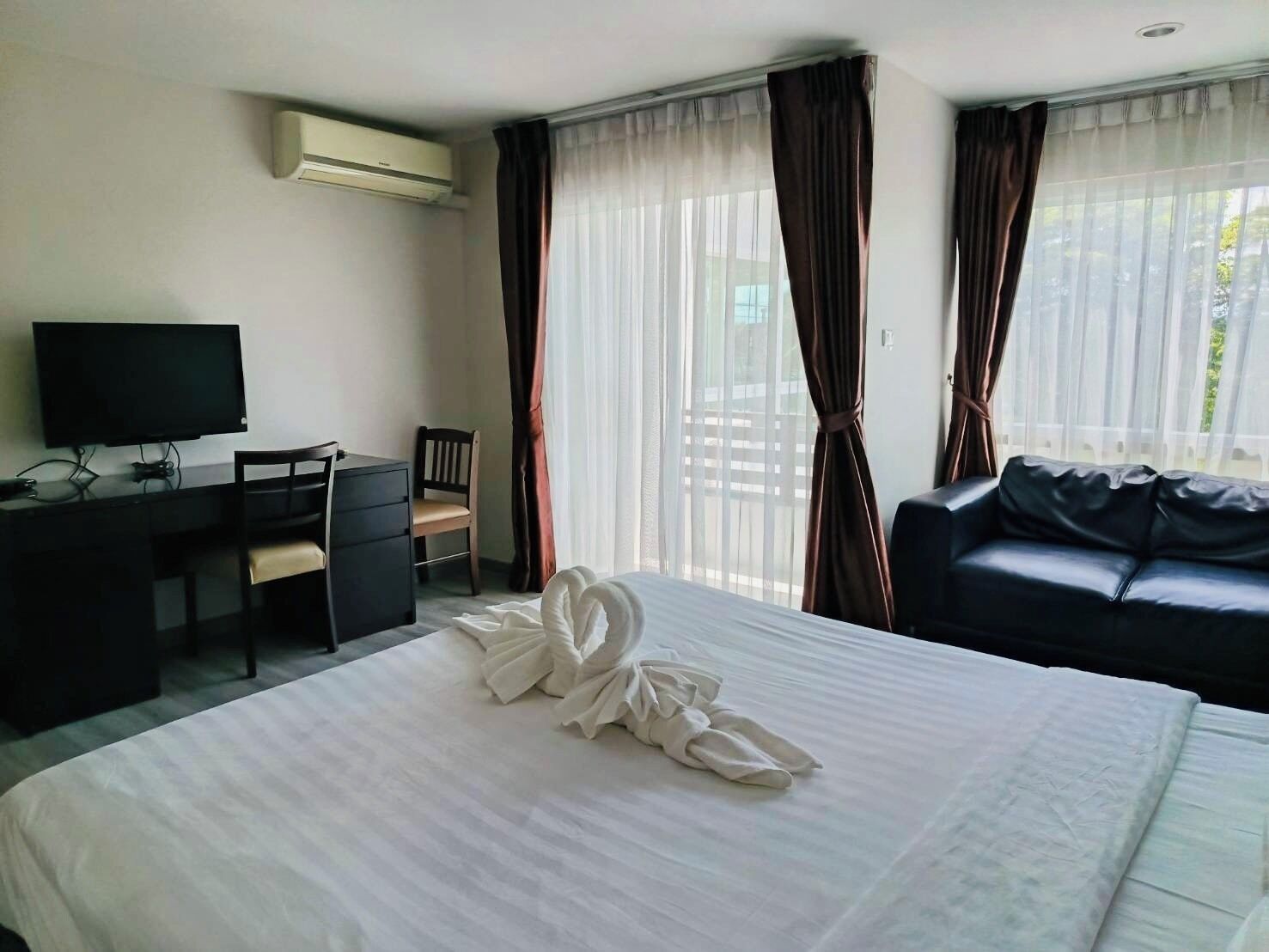 A hotel room with a bed, a desk with a chair, a television, and a sofa.