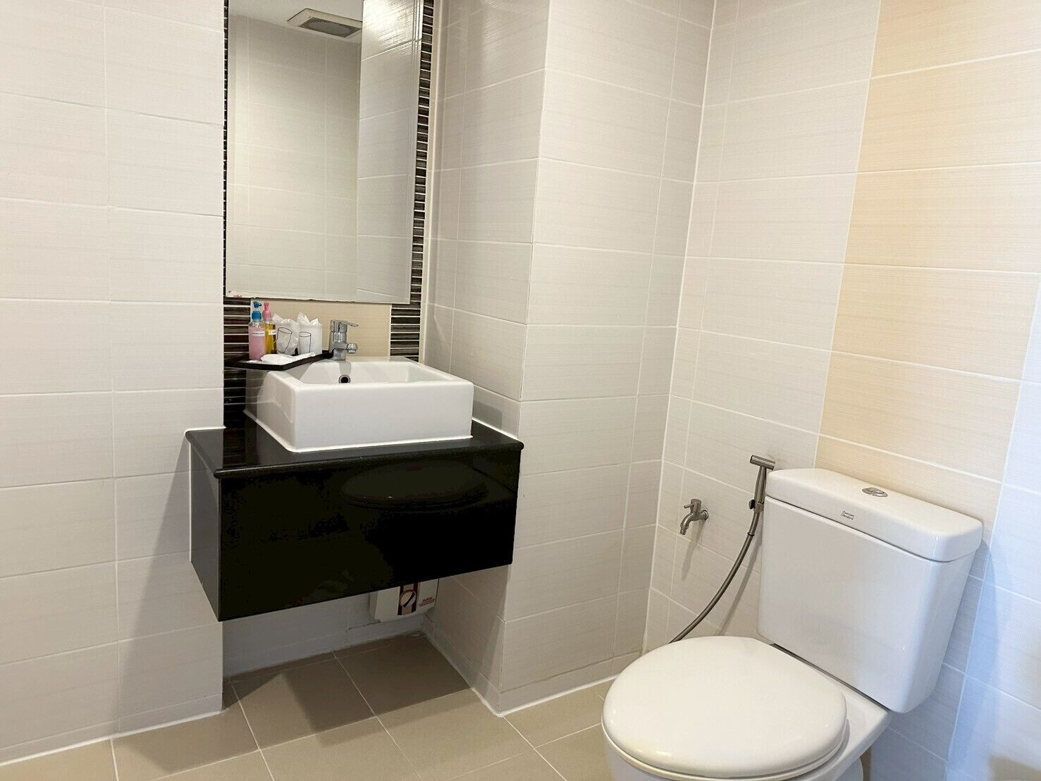 Une salle de bain moderne avec des toilettes blanches, un lavabo noir et un miroir au-dessus du lavabo.
