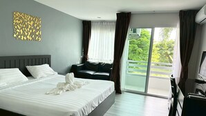 Een moderne hotelkamer met een groot bed, een bank, een bureau en een balkon met uitzicht op groen.
