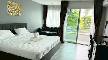 A modern hotel room with a large bed, a sofa, a desk, and a balcony with a view of greenery.
