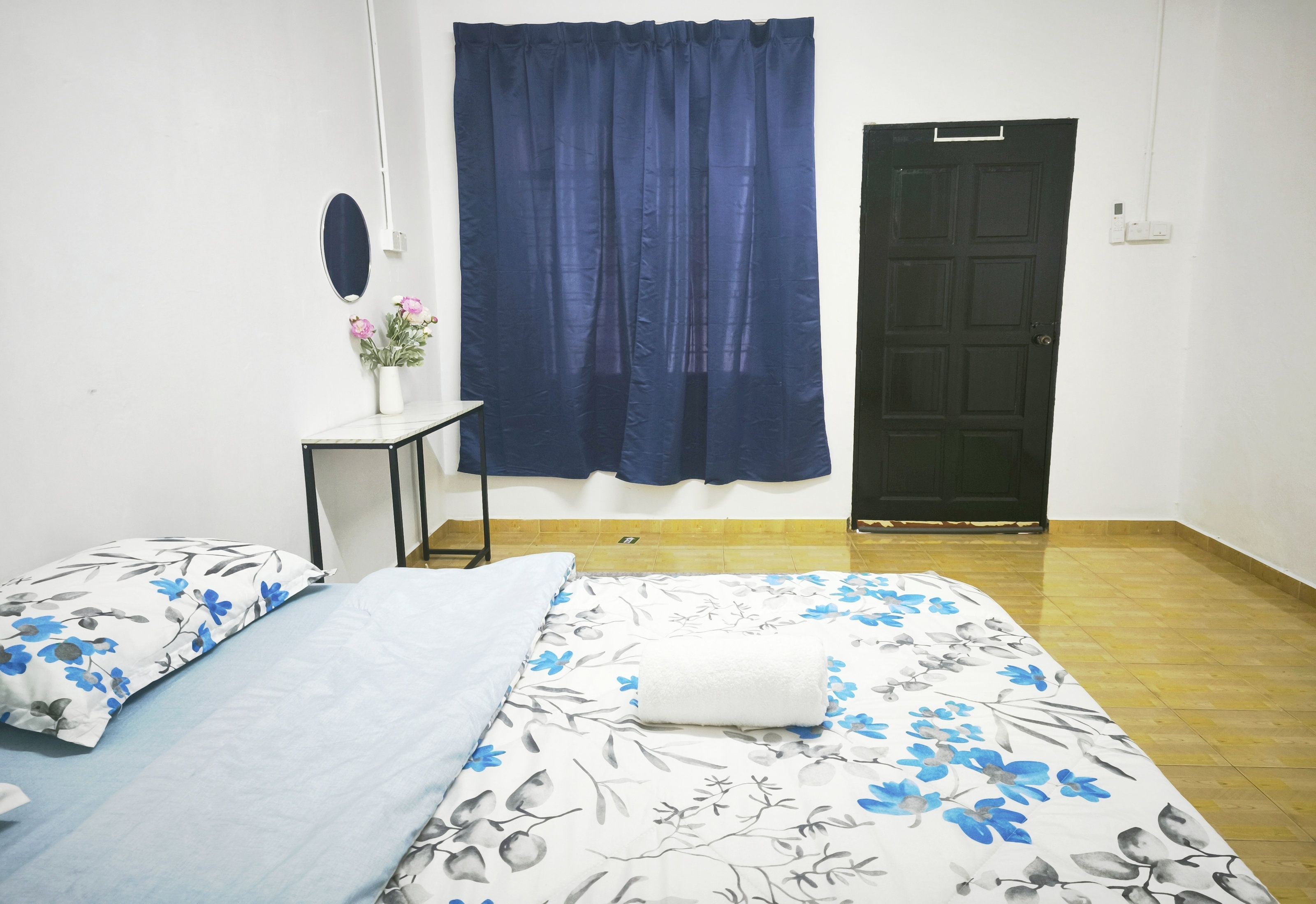 A bedroom with a bed, a small table with a vase of flowers, a blue curtain, and a black door.