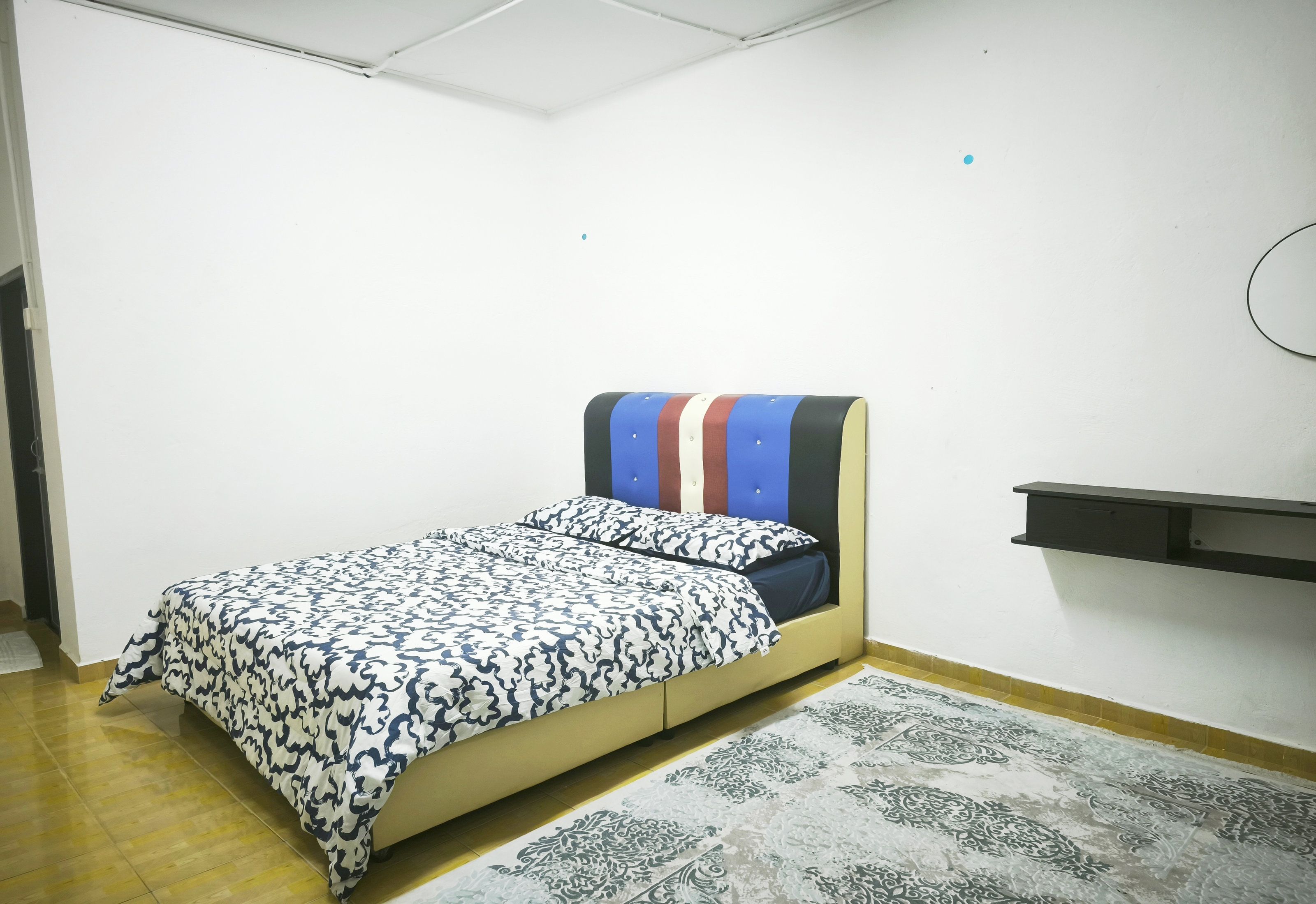 A single bed with a patterned bedspread, a bedside table, and a wall-mounted shelf.