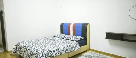 A single bed with a patterned bedspread, a bedside table, and a wall-mounted shelf.