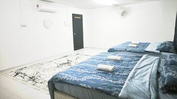 A hotel room with a bed, a bedside table, a wall-mounted air conditioner, a door, and a light switch.