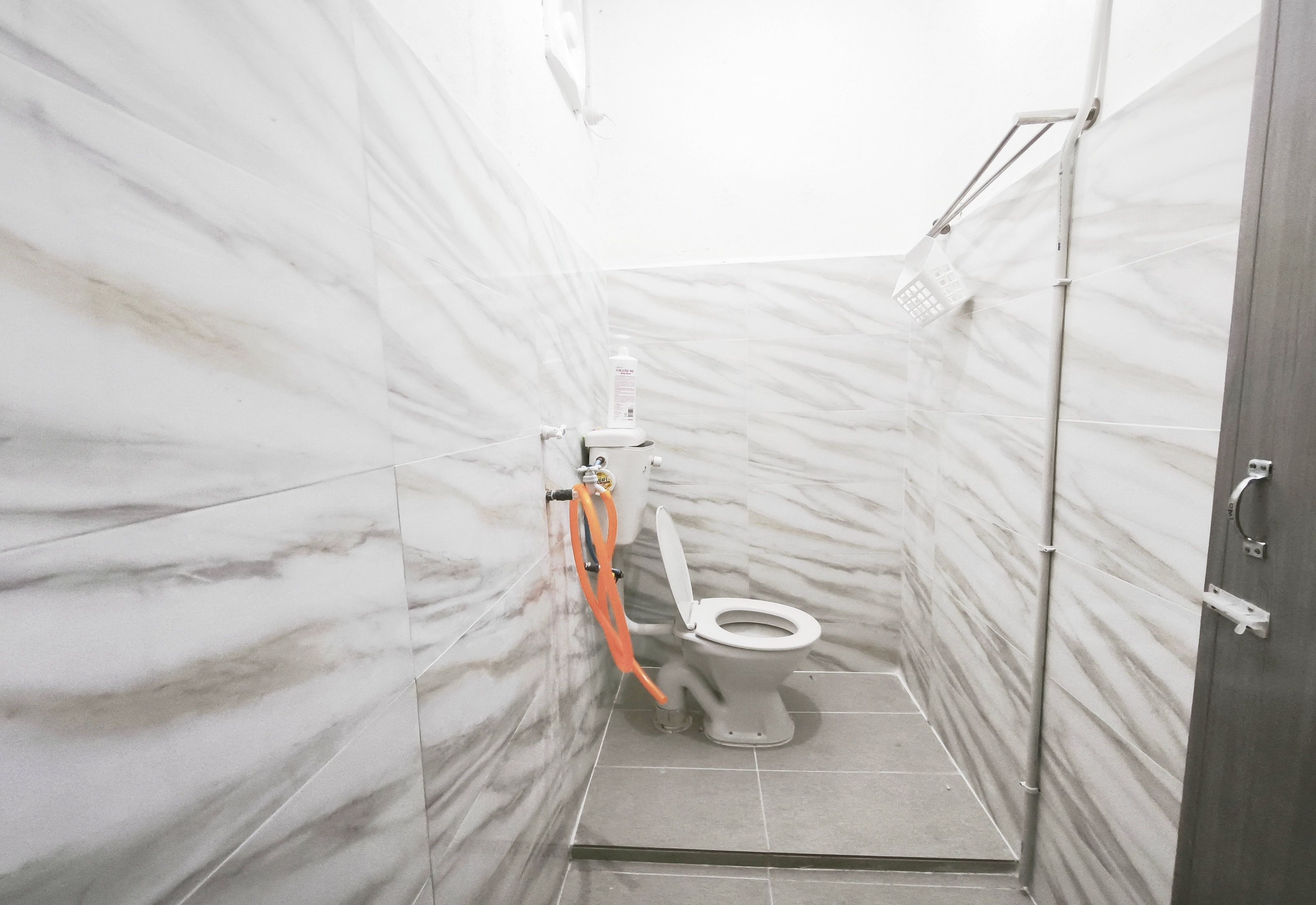 Un baño pequeño y cerrado con inodoro, ducha y pared de mármol.
