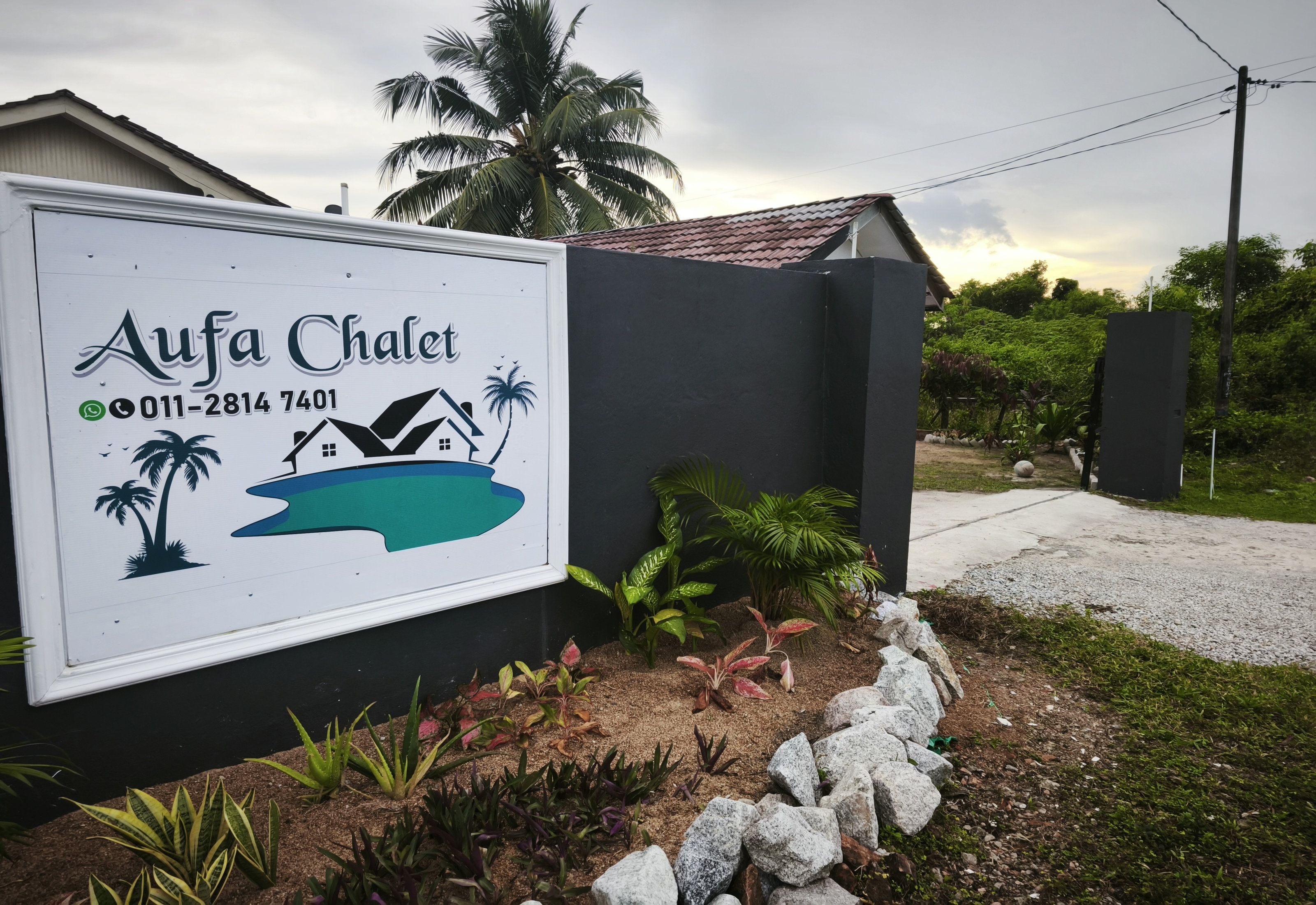 A sign for AuFa Chalet with a contact number, a house graphic, and palm trees.