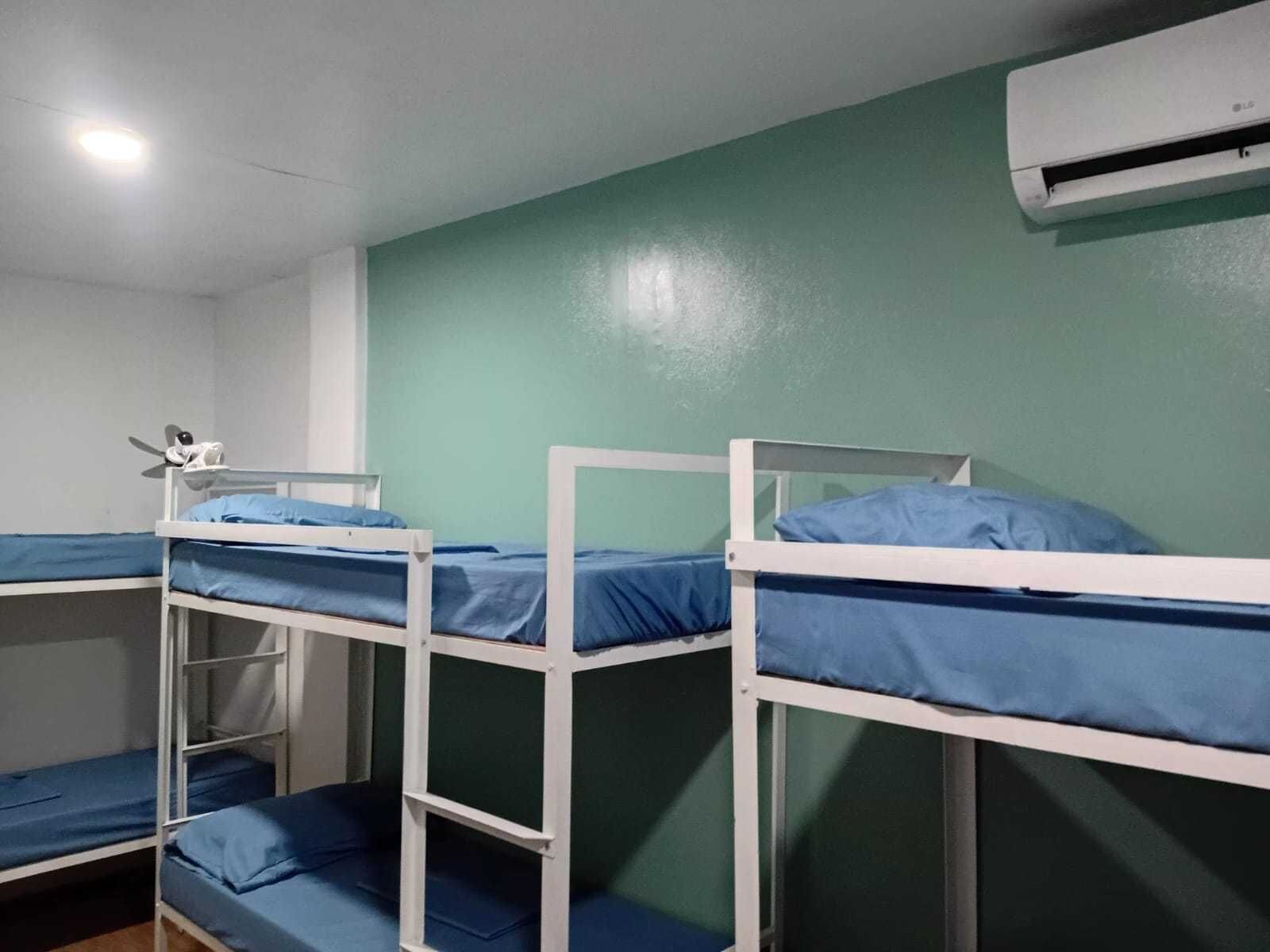 A dormitory room with bunk beds, a ceiling light, and an air conditioning unit.