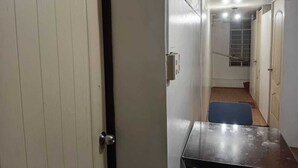 Un couloir étroit, avec une porte marquée du chiffre « 1 » sur le côté gauche, une petite table au centre et un escalier menant à une autre pièce.