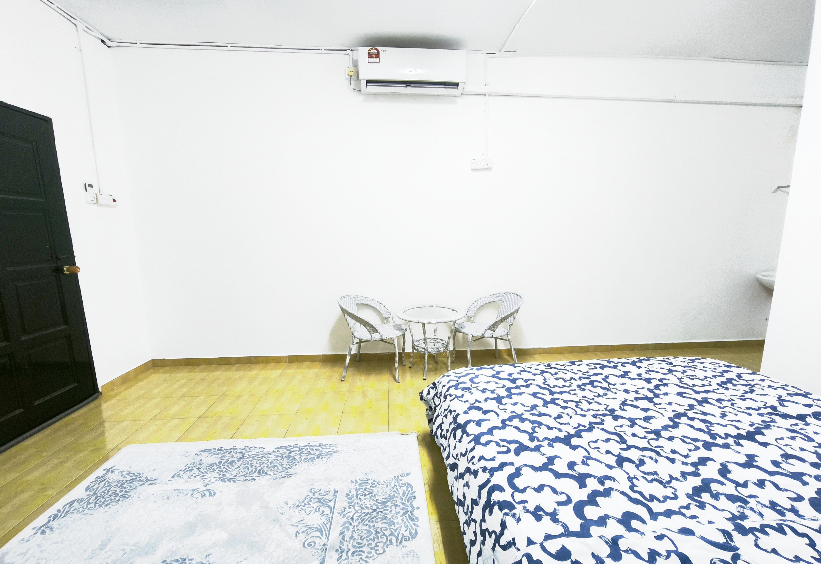 A room with a bed, a small table with chairs, a door, and an air conditioning unit on the wall.