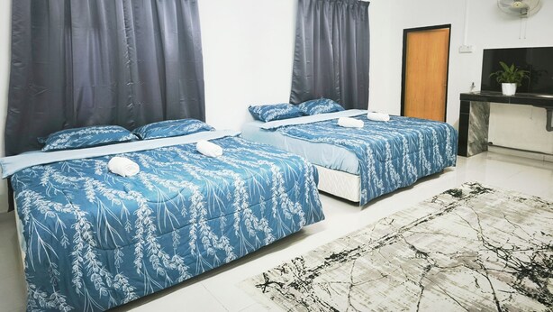 Une chambre d’hôtel avec deux lits, des rideaux foncés, un petit bureau avec une plante et un mur blanc.