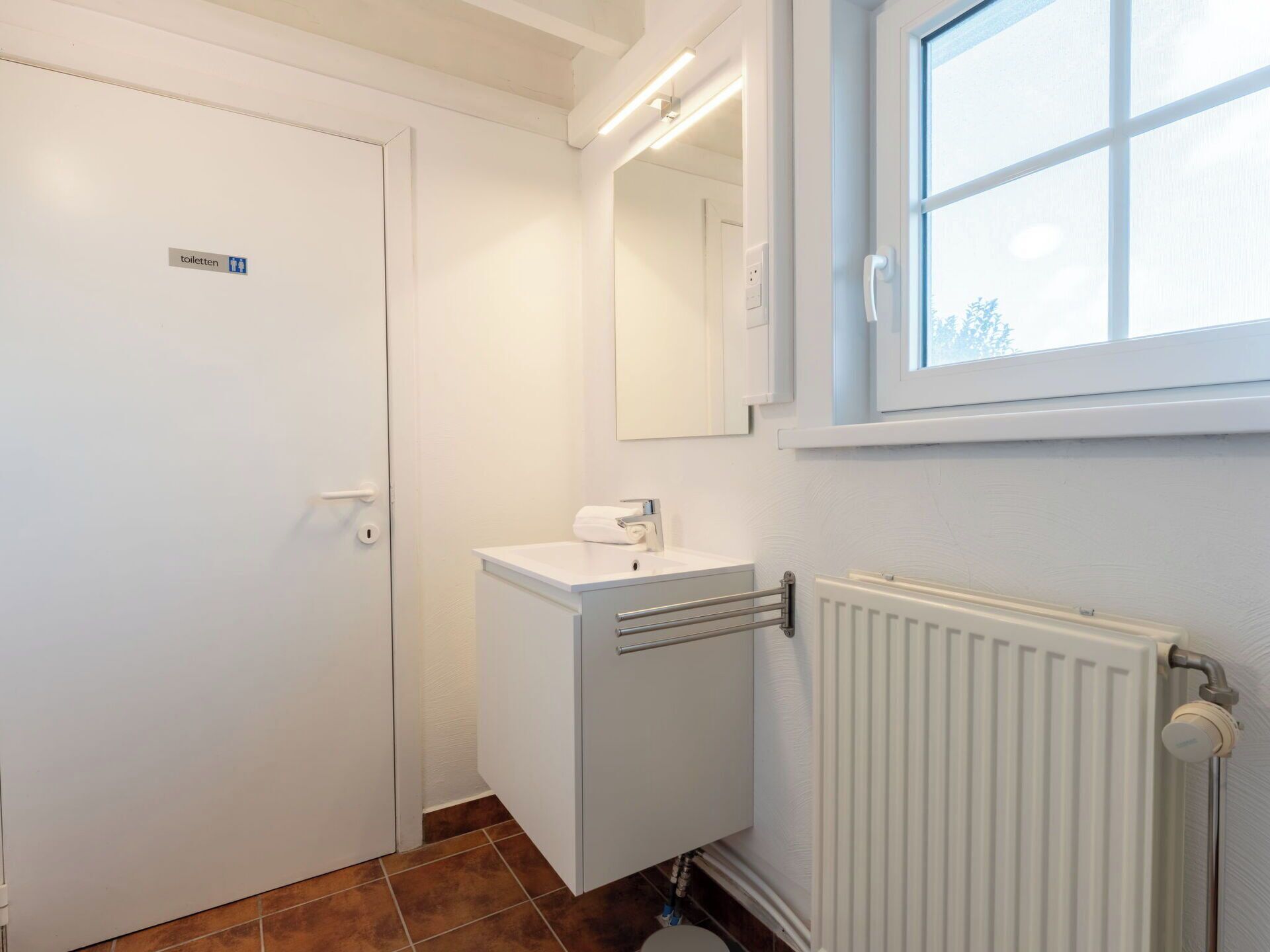 Une petite salle de bain avec un lavabo blanc, un miroir et un radiateur.