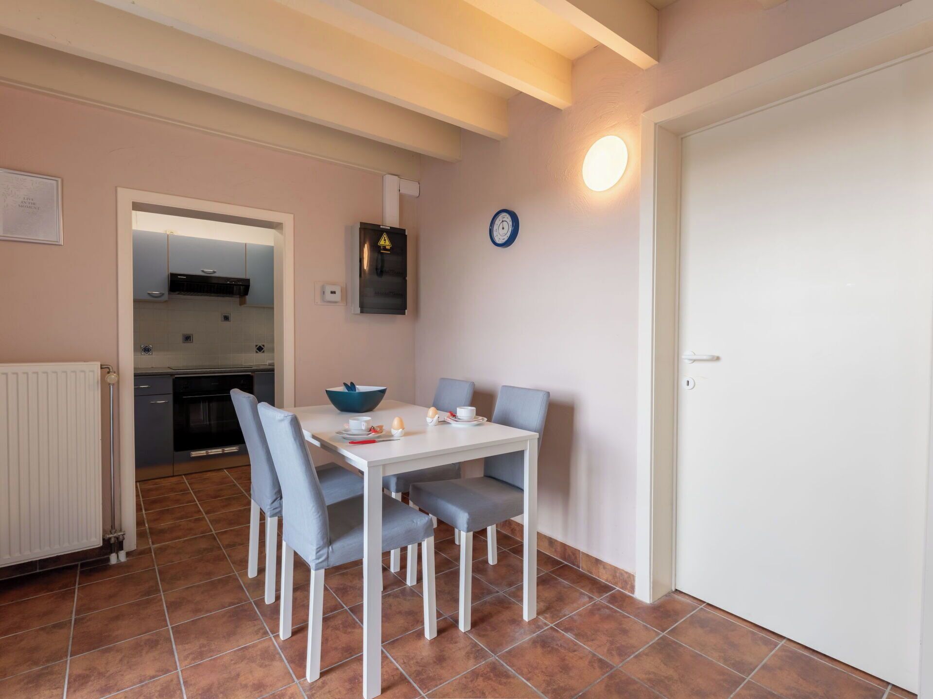 Een kleine keuken met een eethoek, een witte deur en een klok aan de muur.
