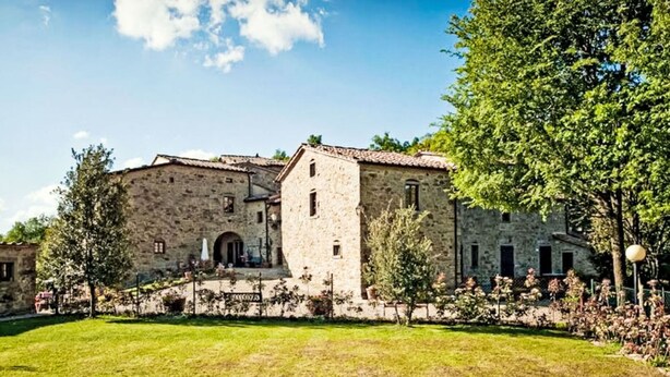A stone building with a central tower, surrounded by a well-maintained lawn and trees.