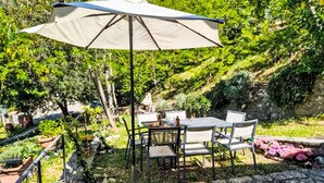 An outdoor patio with a table and chairs, surrounded by greenery and a stone pathway.