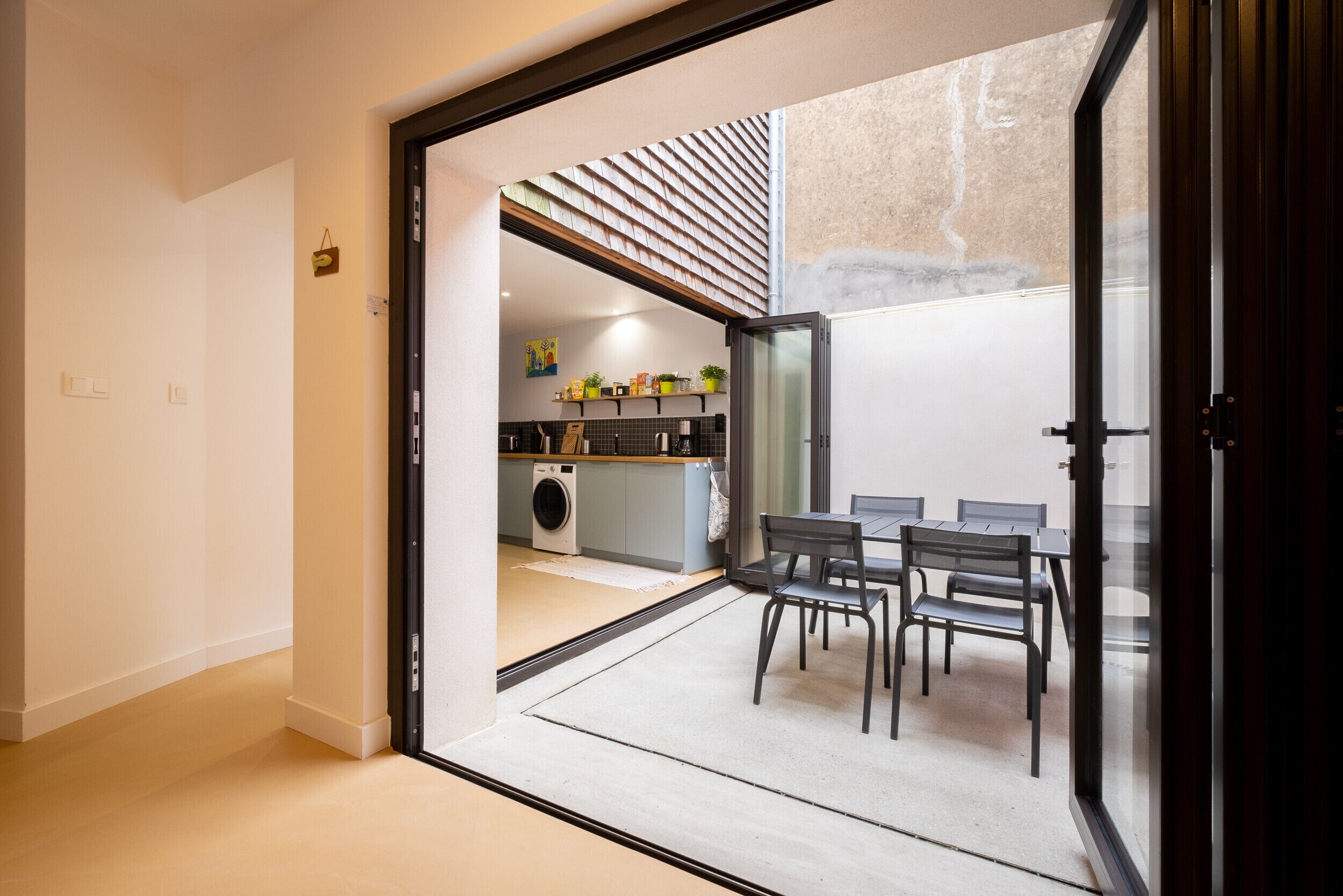 A modern kitchen with a built-in washing machine, a dining area with a table and chairs, and a large sliding glass door leading to an outdoor space.