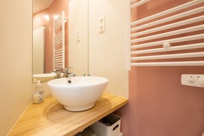 Ein Badezimmer mit einem weißen Waschbecken, einem Spiegel, einem Handtuchhalter und einer Seifenspender.