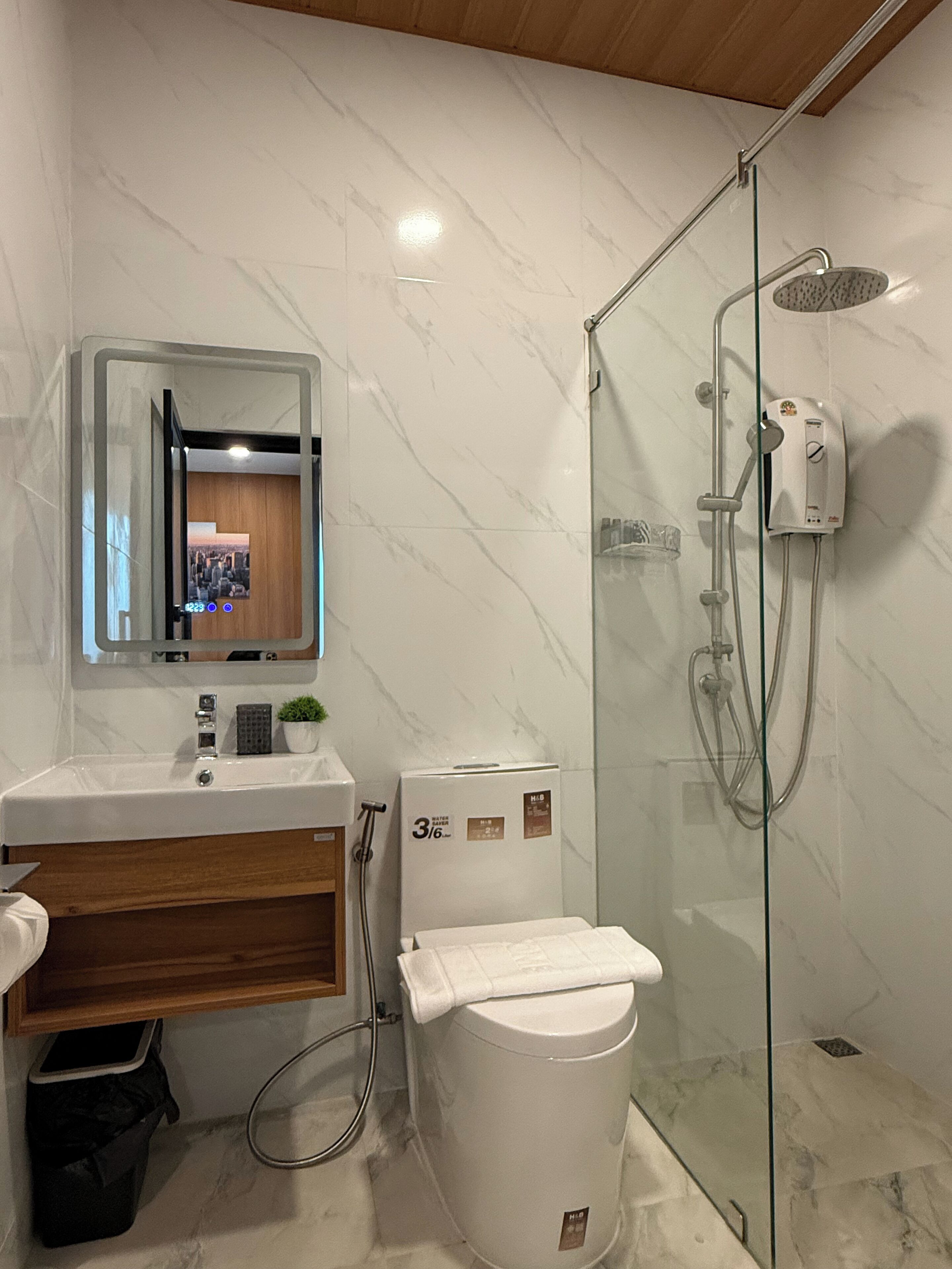 Ein modernes Badezimmer mit einer Glaskabine zur Dusche, einer weißen Toilette und einem Waschbecken mit Spiegel darüber.