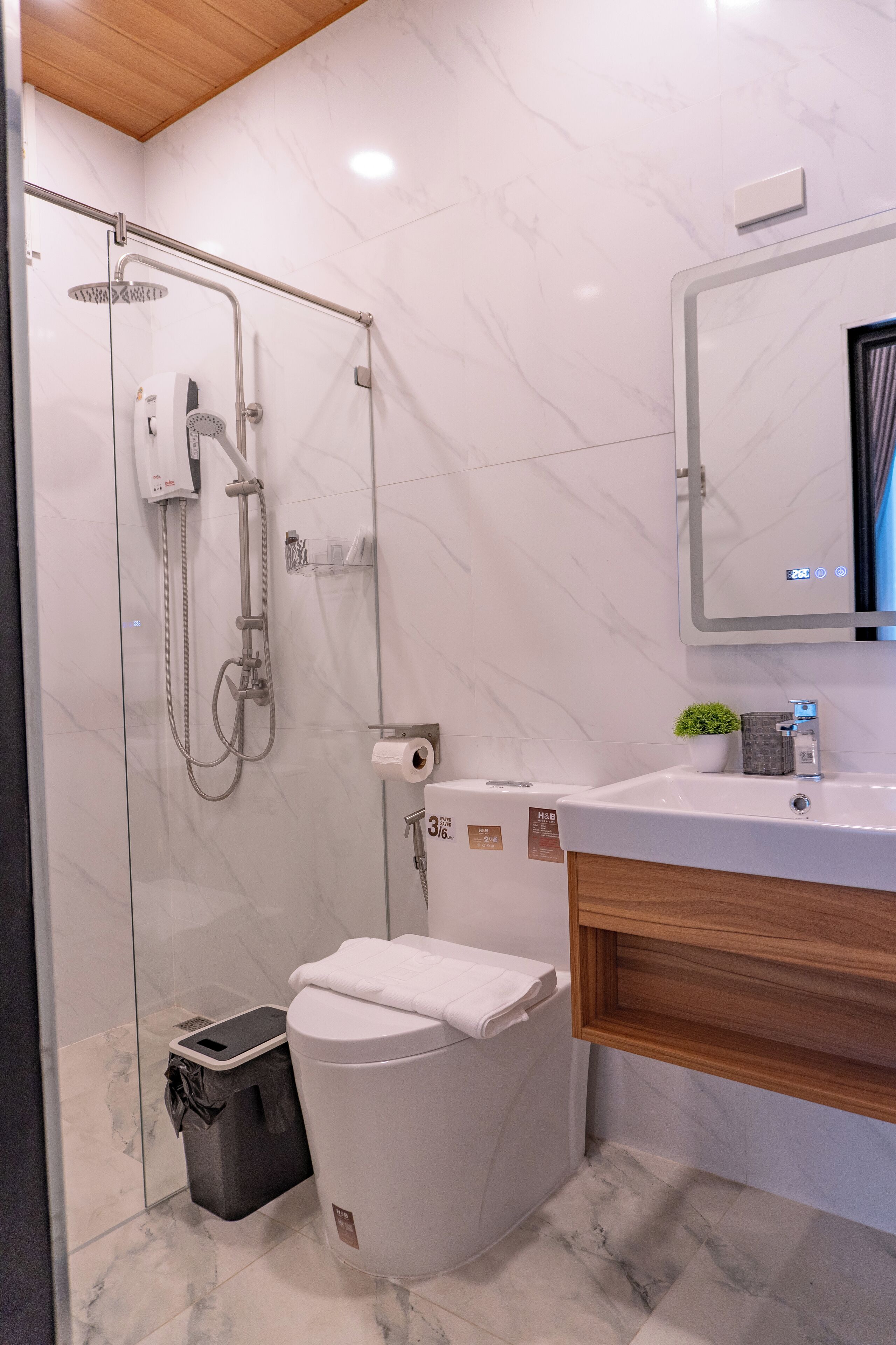 Ein modernes Badezimmer mit einer ein Glasfach raumseitig geschlossenen Dusche, einer weißen Toilette und einem hölzernen Waschtisch mit Spiegel.