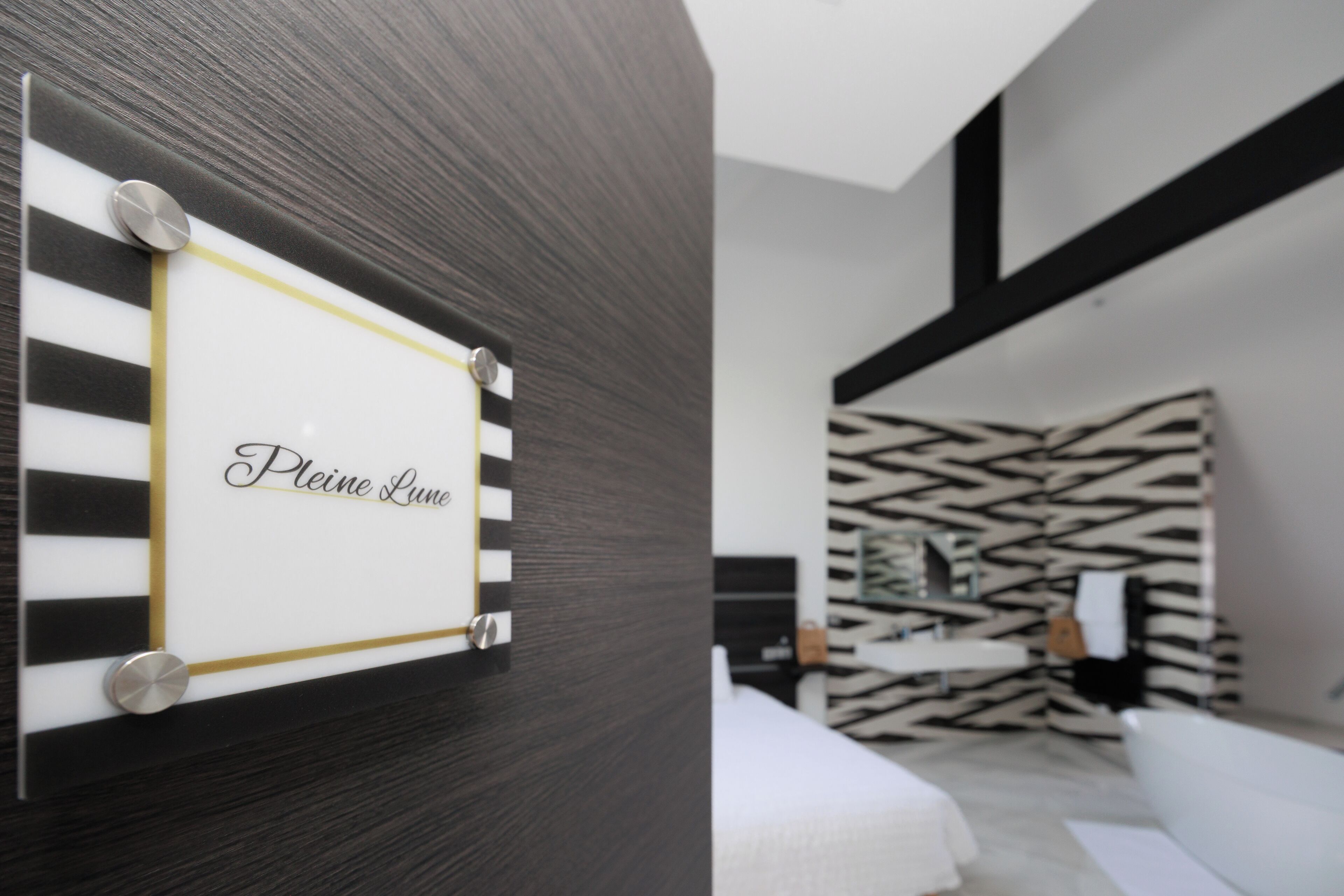 A modern room with a black and white striped wall, a bed, and a wall-mounted sign that reads "Please Leave."