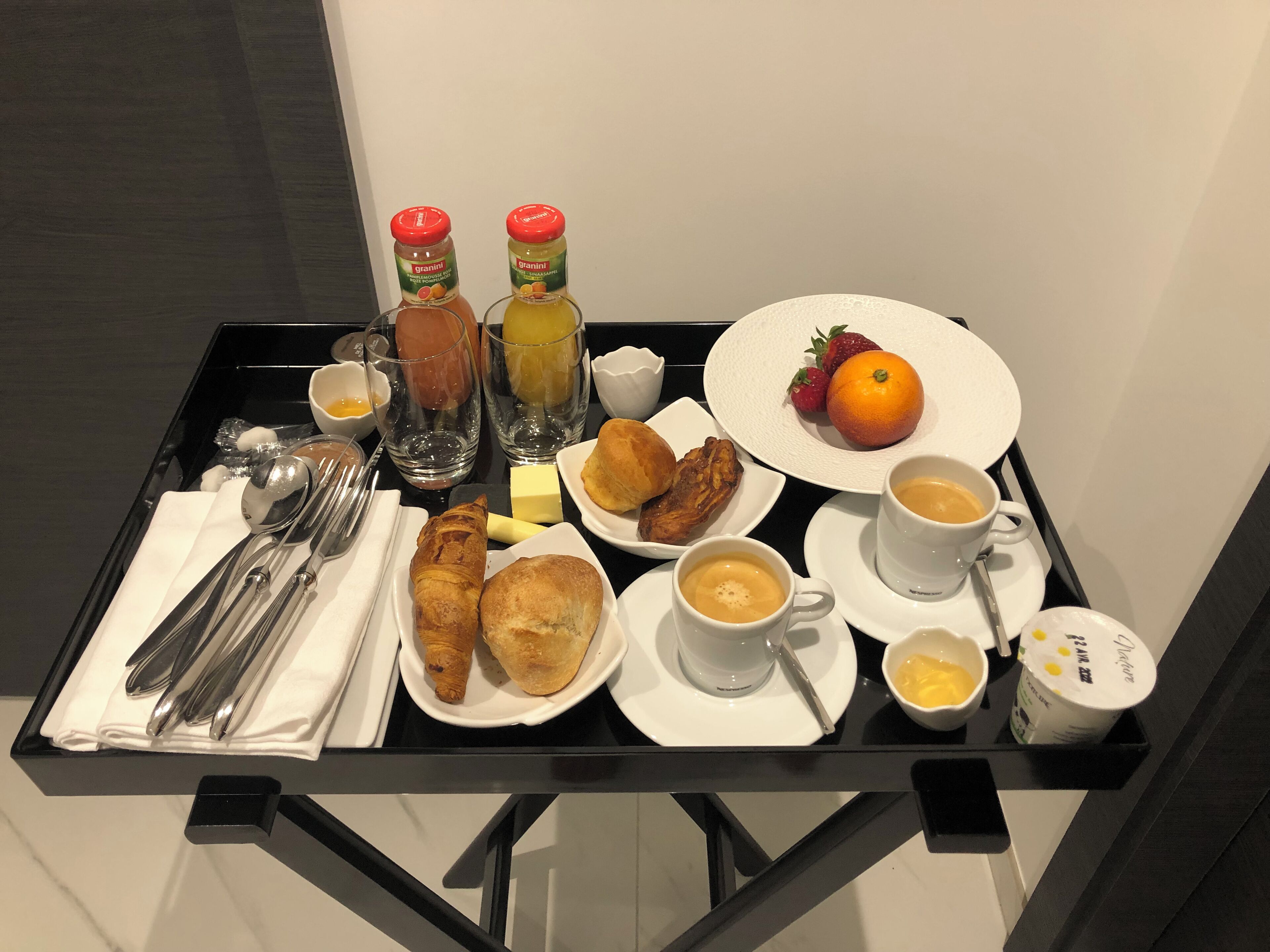Ett frukostbricka med croissanter, bakverk, frukt, kaffe och juice.