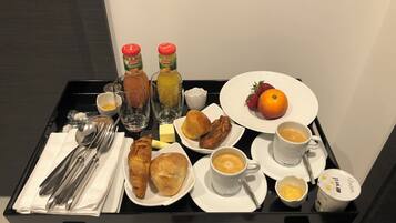 Ett frukostbricka med croissanter, bakverk, frukt, kaffe och juice.