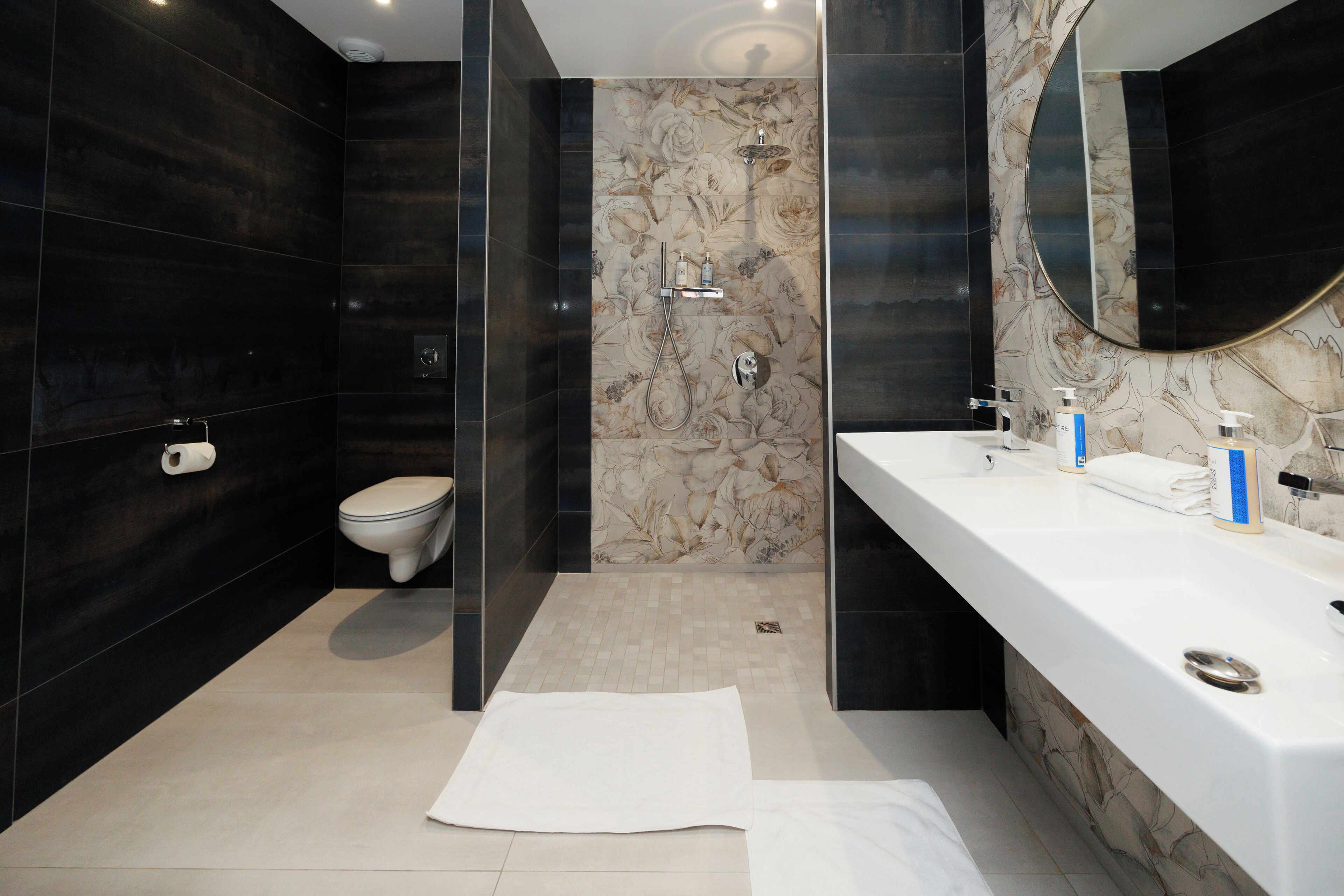A modern bathroom with a toilet, shower, and a large mirror above the sink.