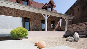 Un bâtiment en pierre avec un toit recouvert de tuiles rouges, un patio abrité et un petit arbuste vert.